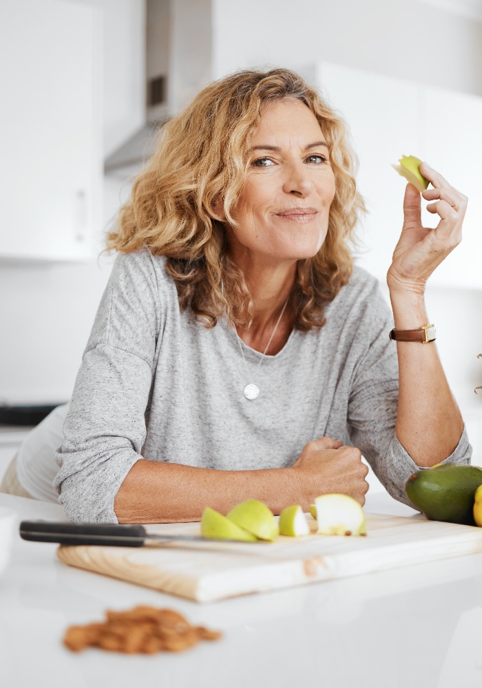 Porträt, Obstsalat und Apfel mit einer älteren Frau in ihrer Küche zu Hause, zum Thema Gesundheit, Ernährung oder Diät. Lächeln, Essen und Kochen mit einer glücklichen, reifen Rentnerin, die sich zu Hause gesund ernährt.