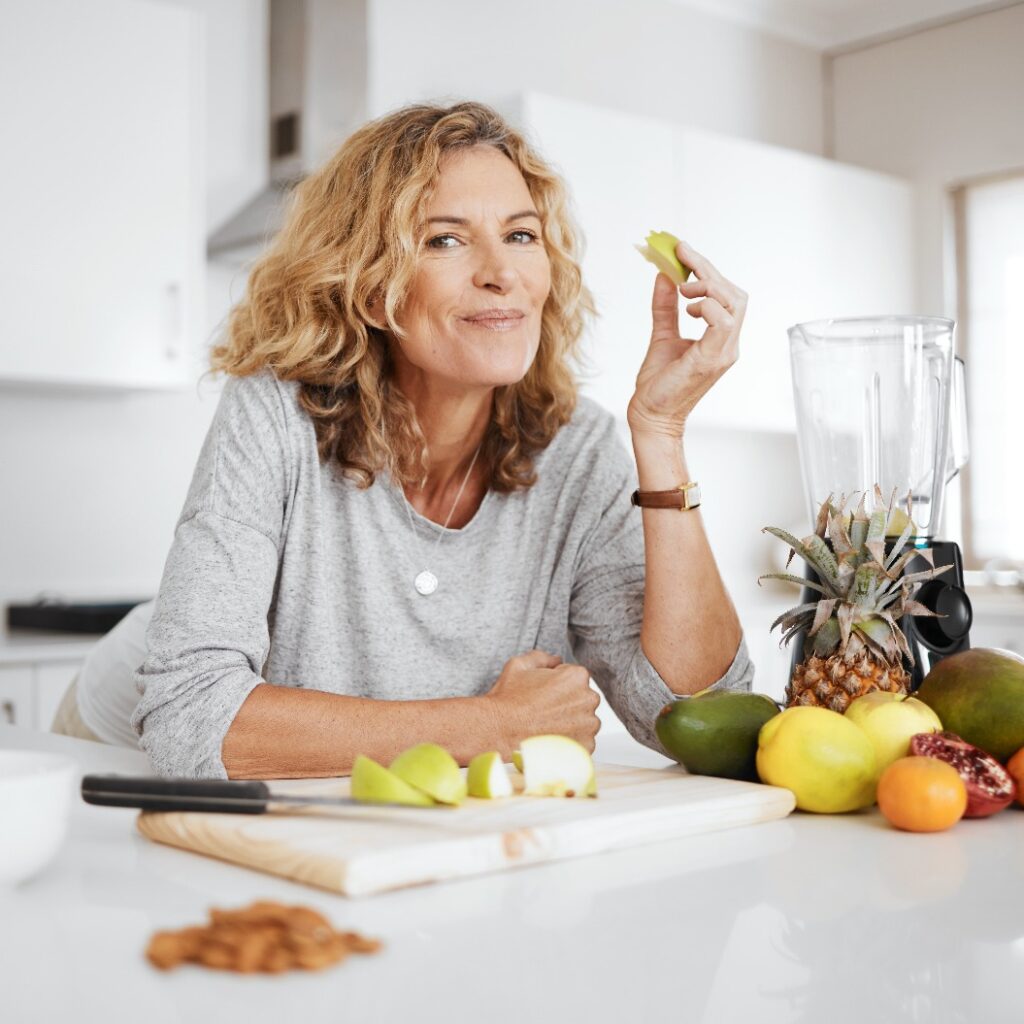 Porträt, Obstsalat und Apfel mit einer älteren Frau in der Küche ihres Zuhauses – Thema Gesundheit, Ernährung oder Diät. Lächeln, Essen und Kochen mit einer glücklichen, reifen Rentnerin, die sich zu Hause gesund ernährt