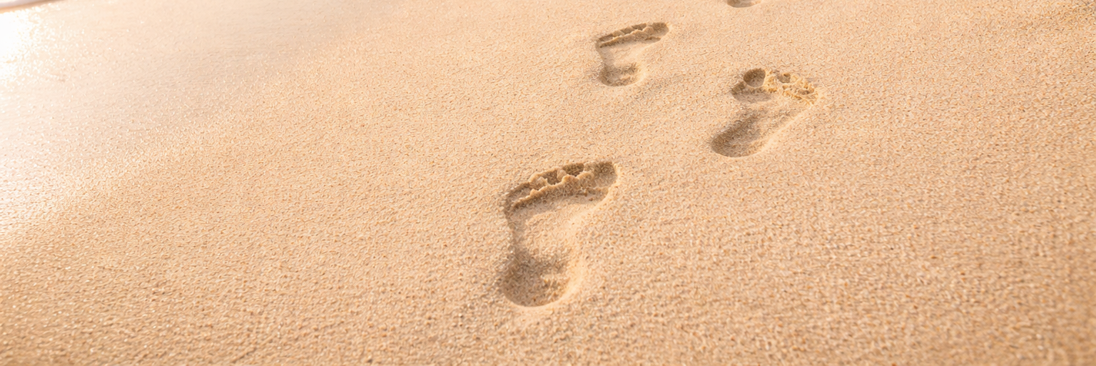 Spuren von nackten Füßen im hellen Sandstrand führen am türkisfarbenen Meer entlang